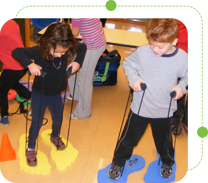 Two children are standing on the floor with a pair of ski poles.