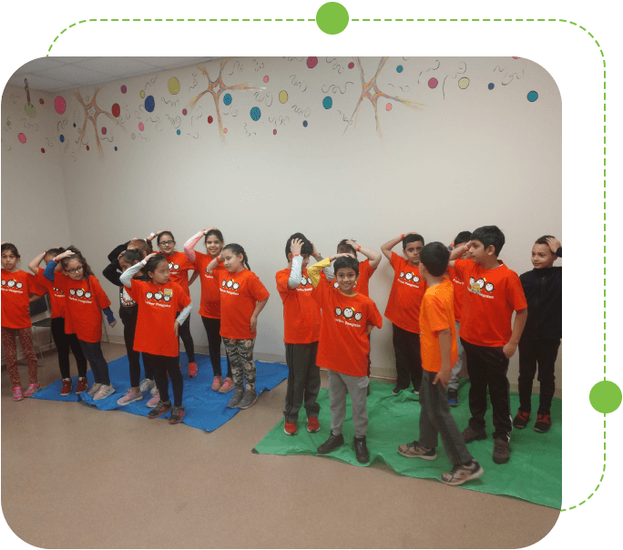 A group of children in orange shirts standing on green mats.