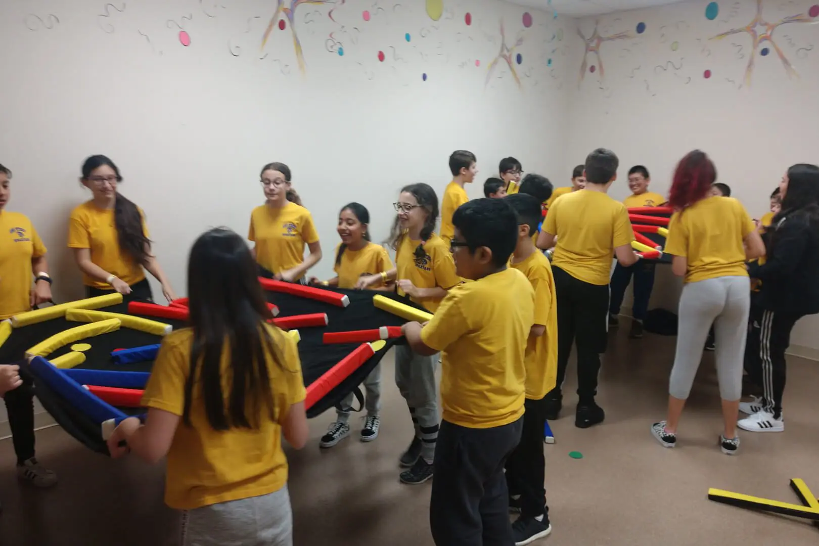 A group of children in yellow shirts holding red sticks.