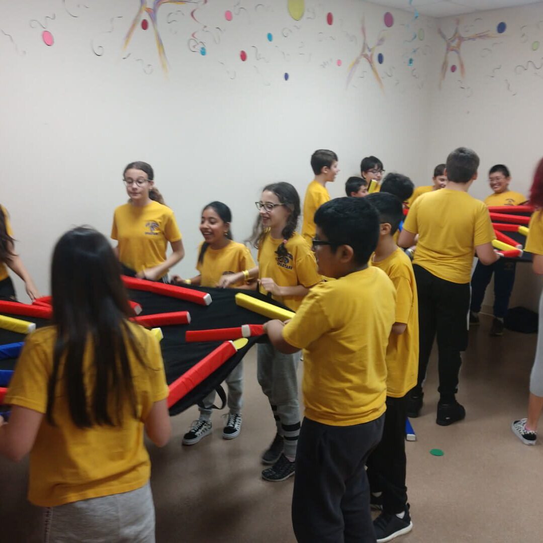 A group of children in yellow shirts holding red sticks.